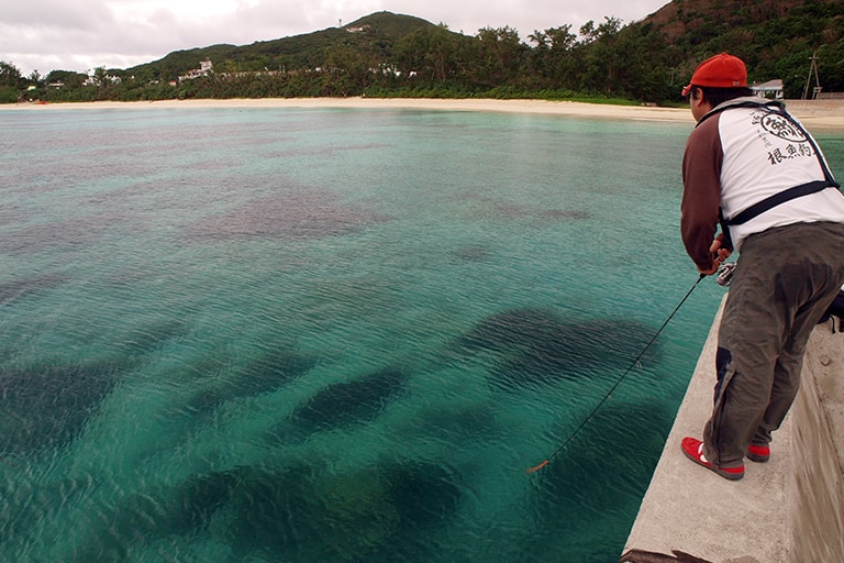 透明度抜群の沖縄の海。足もとには真新しい墨跡。エギングロッド1本を持参して餌木を投げたりルアーを投げたりするだけのお手軽釣り旅もアリ！