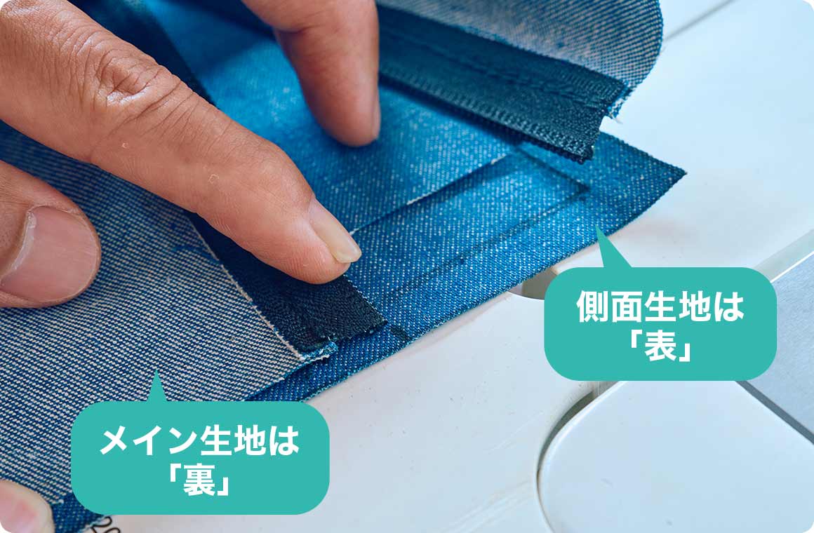 メイン生地と側面生地を縫い付ける作業。側面生地を表にし、その上にメイン生地を裏にして配置。縫う際にスライダー（金具部分）が邪魔にならないようにジッパーを少し開き、側面生地の印を付けた箇所と合わせて、縫い始める。