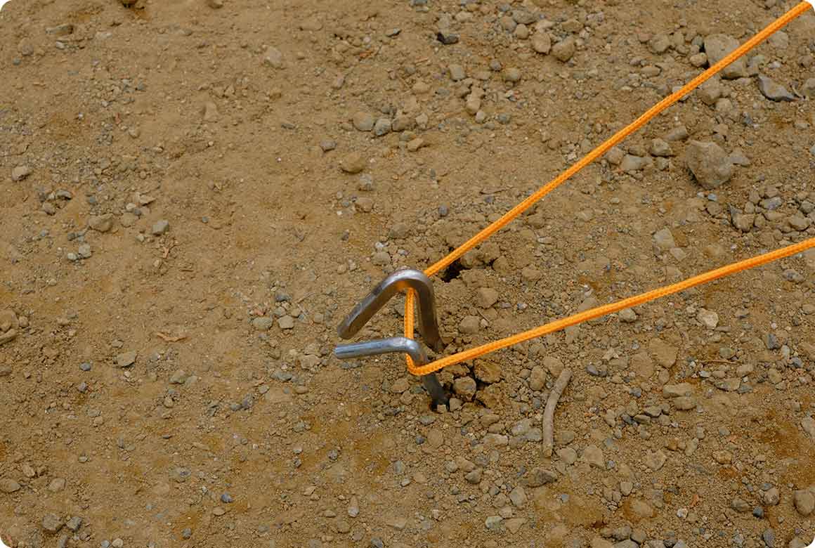 張り綱が抜けるとテントやタープのバランスがくずれるので、いつものペグにもう1本長いペグを追加して補強します。2本のペグを地表でクロスさせるようにすれば、万一どちらかのペグが抜けても張り綱の長さは大きく変わりません。抜けたことに気づいたら、落ち着いてもう一度ペグをしっかり差し込みましょう。