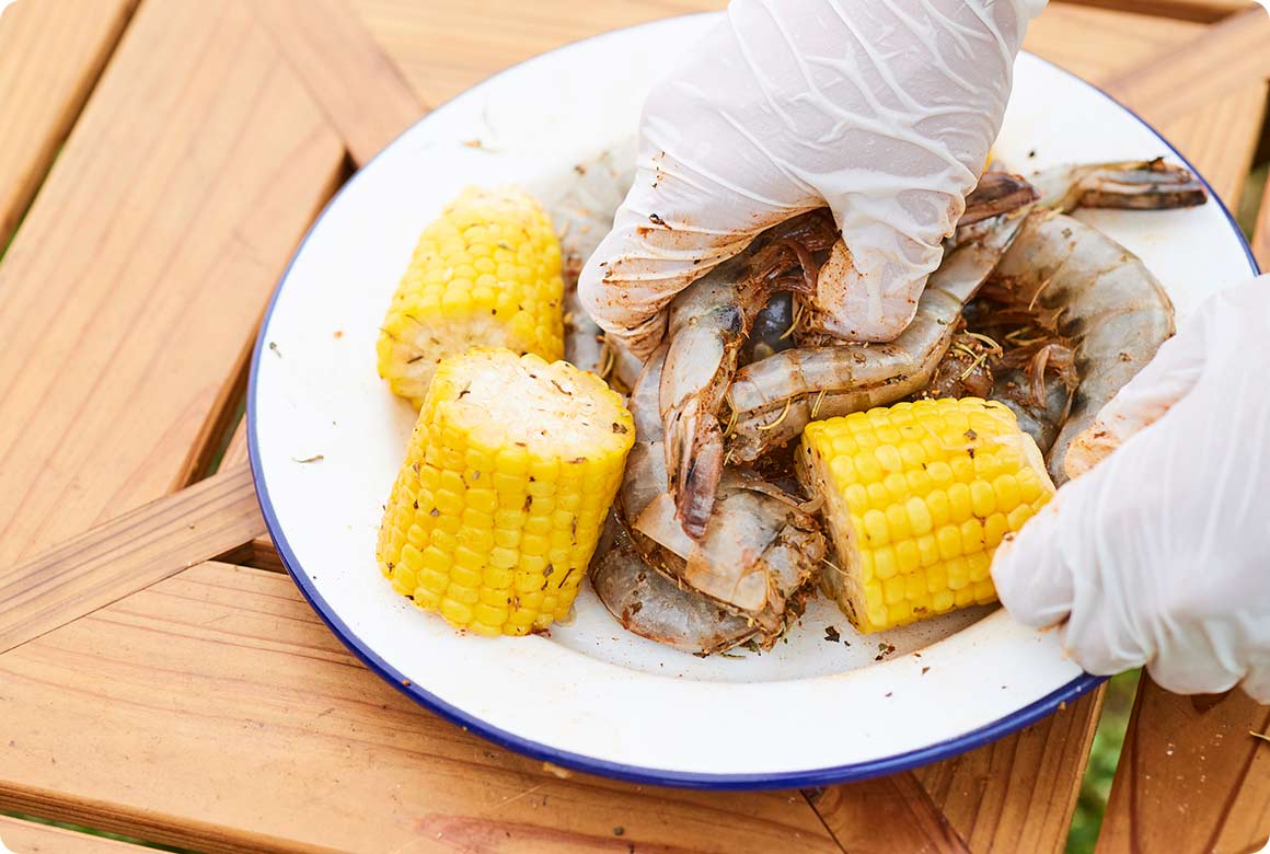 下処理をしたエビ、ゆでとうもろこしと、パプリカパウダーやカイエンペッパーなどのスパイス、調味料をマリネする