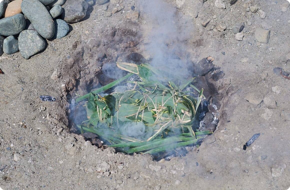 地面に掘った穴に笹の葉を敷き、鶏肉を入れる画像