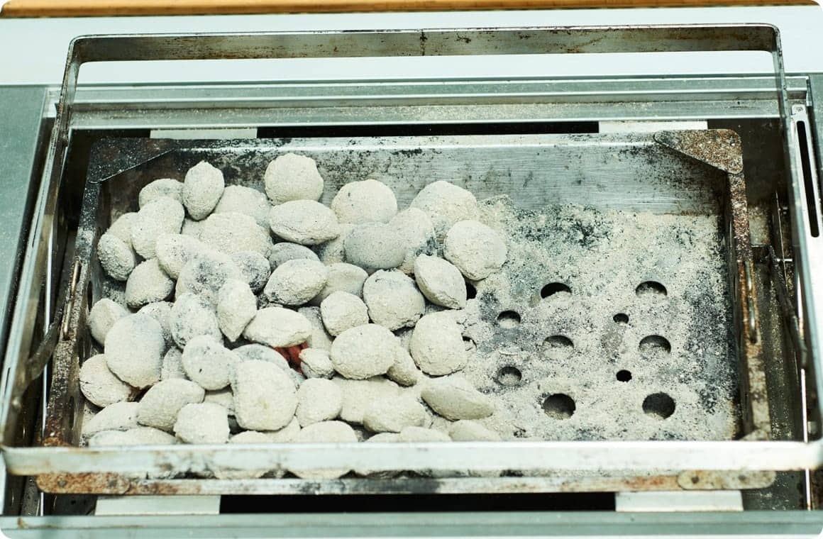 グリルの半分に寄せて置かれた炭の画像