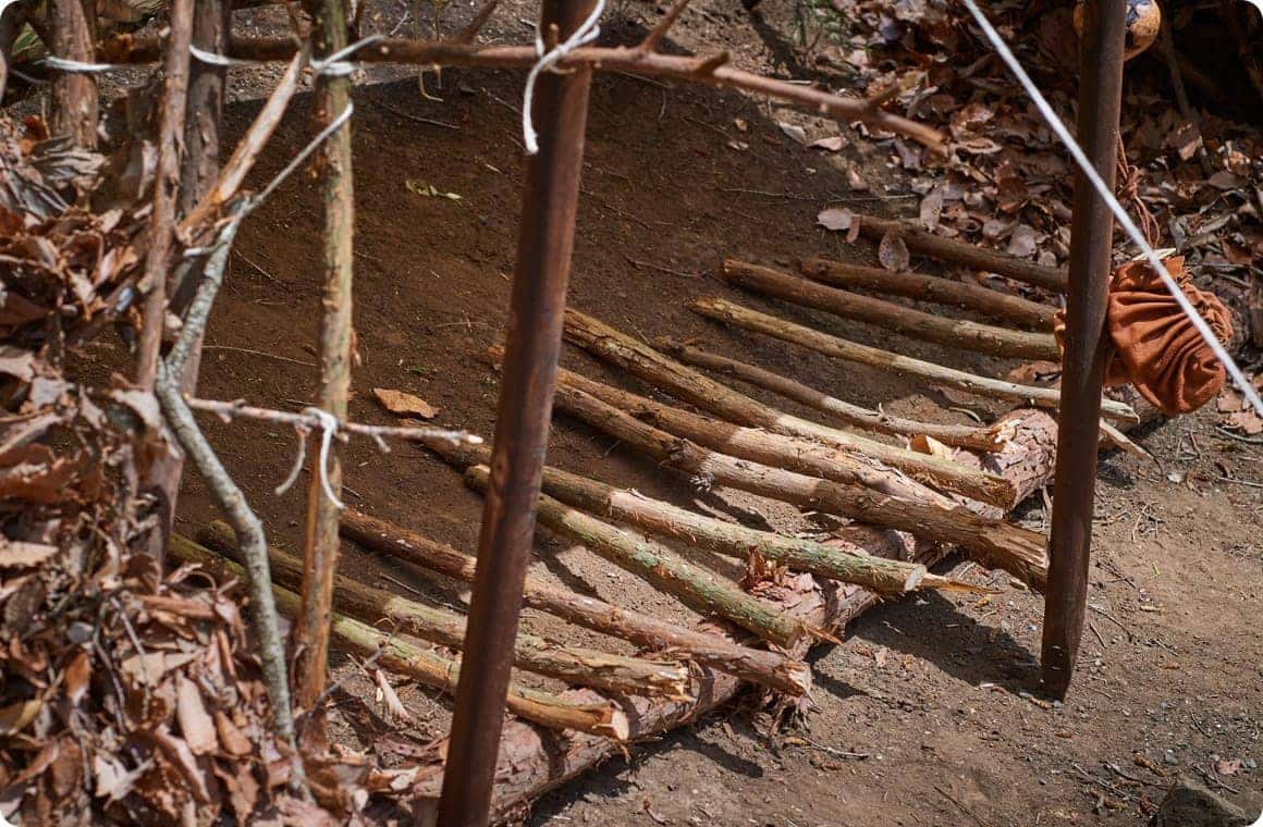 長めの木を横に置いた後、その木に対して垂直に長めの枝を10本ほど並べた画像