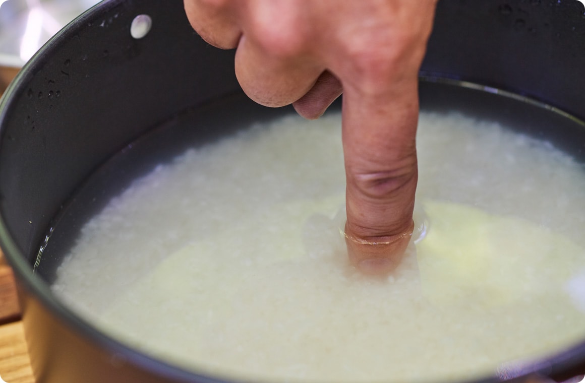 米と水を入れた鍋に人差し指を入れる画像