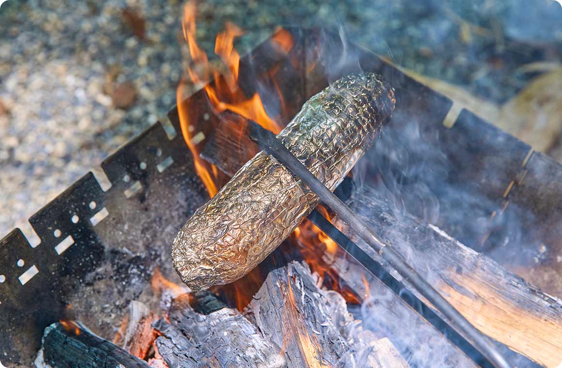 アルミホイルで巻いたとうもろこしを直火で焼く画像