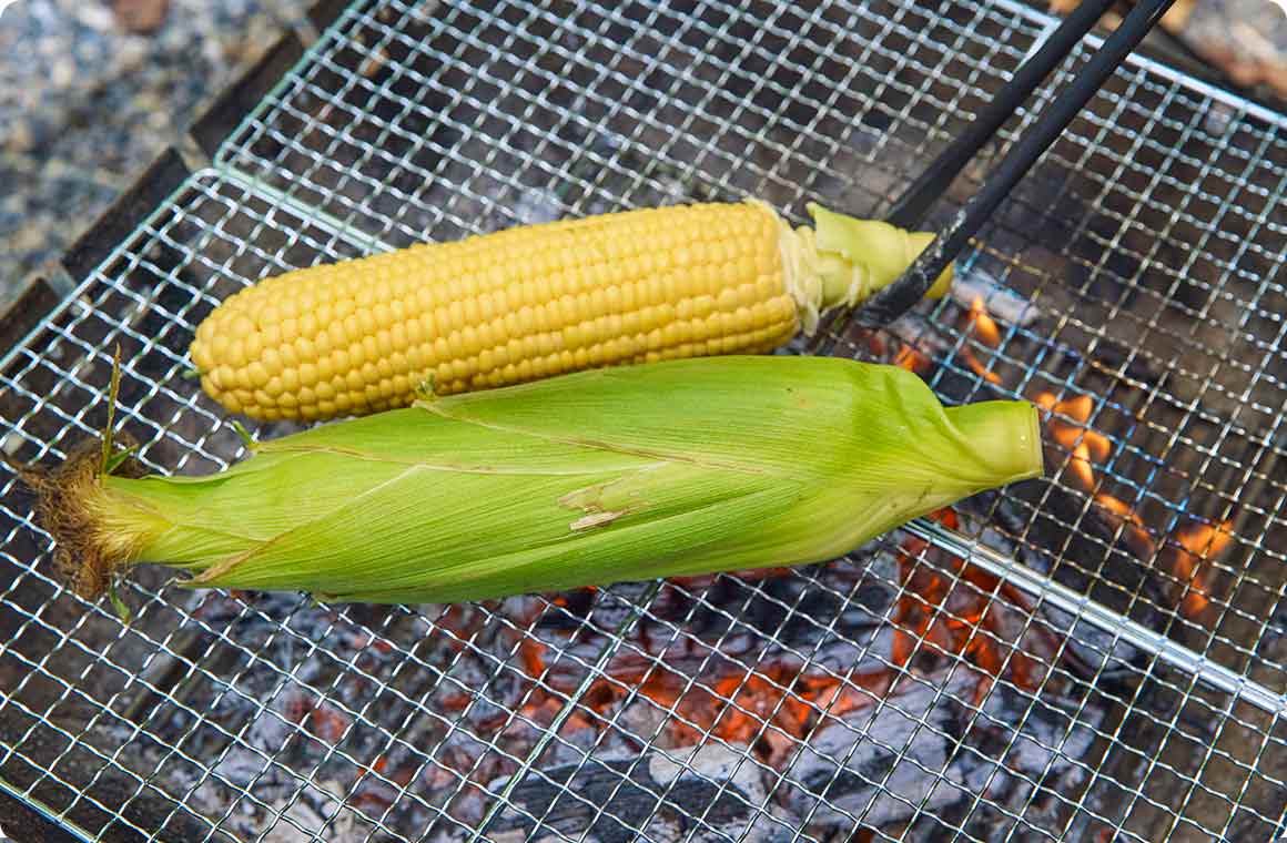 とうもろこしを遠火にした焼き網の上で焼く画像