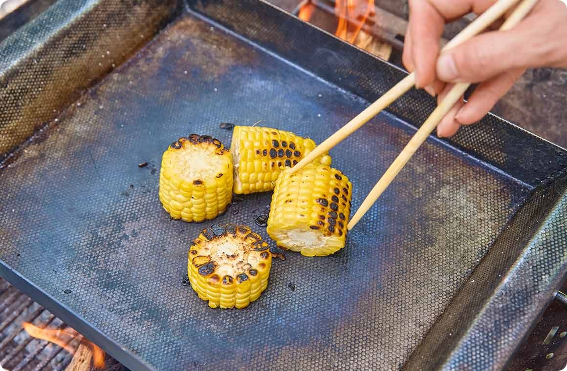 皮をむいたとうもろこしを鉄板で焼く画像