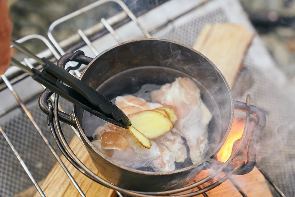 ダッチオーブンに水と手羽元、長ネギ、スライスした生姜を入れて火にかける