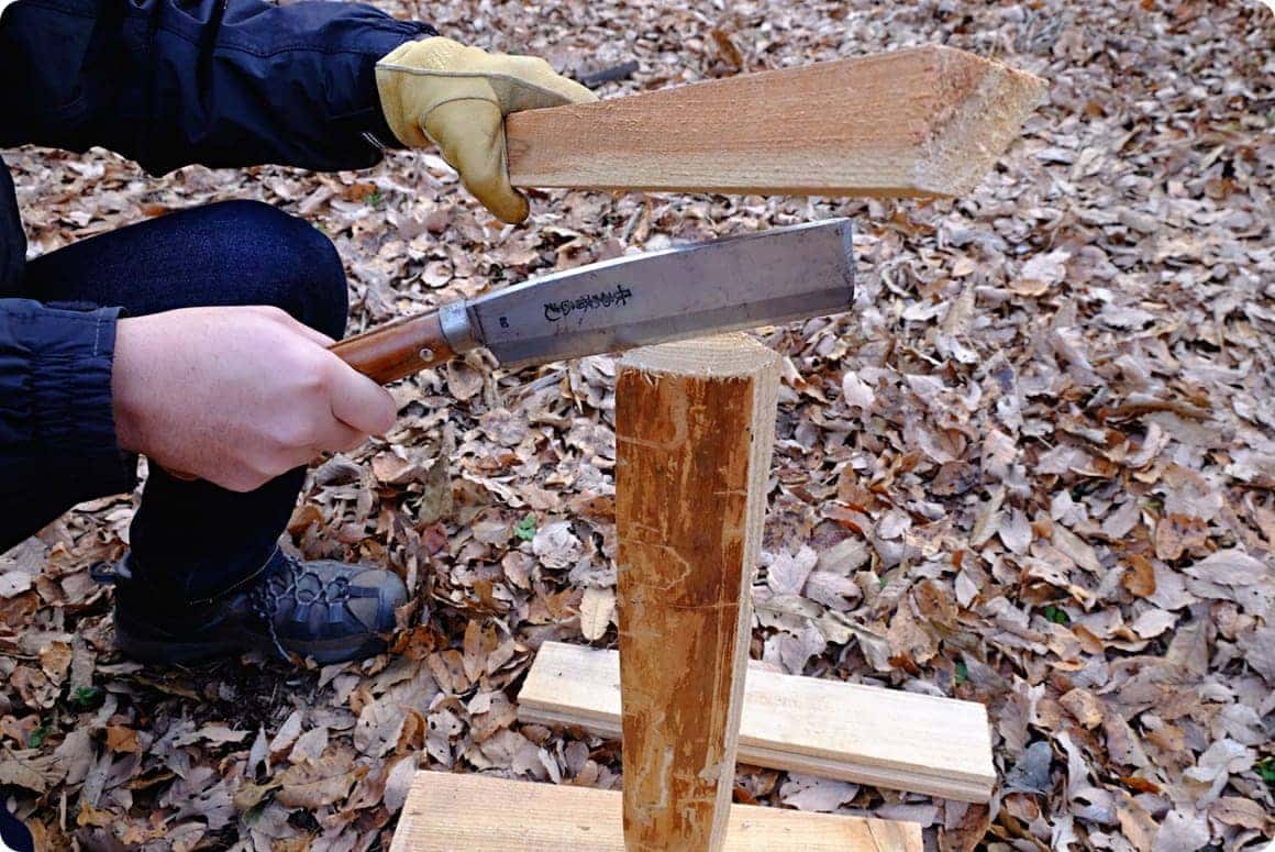 台に薪を立て、薪の上にナタを添える。ナタの背を太めの薪で、たたきます