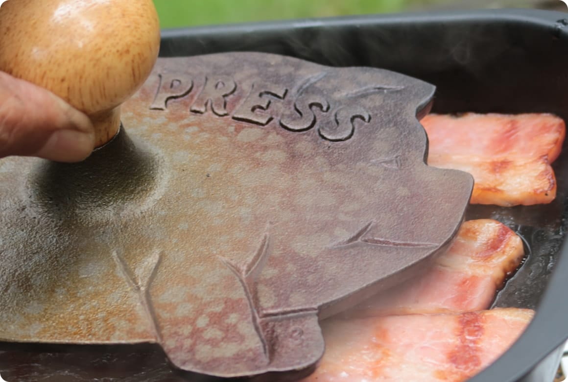 ベーコンやチキンをアツアツのダッチオーブンやスキレットに乗せ、その上からプレスする