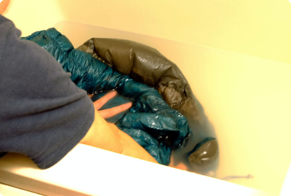 寝袋をたたみ、空気を抜きながら寝袋全体をぬるま湯に沈めます