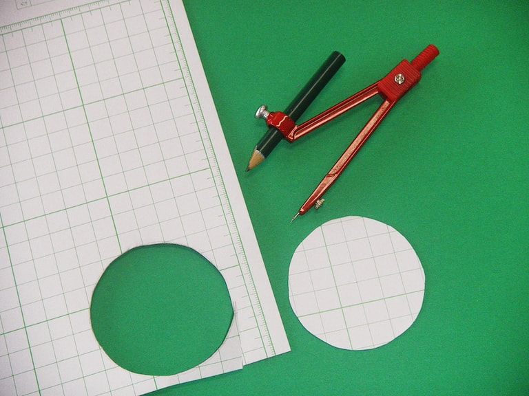 コンパスであつ紙に丸い形をかき、はさみで切りとる。
