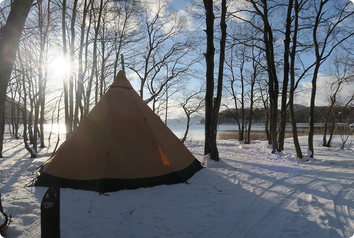 湖畔沿いの木々の中で楽しむ雪中キャンプ。朝目覚めて外を見ると、湖と雪に反射した陽の光に包まれ、雪中キャンプならではの独特な雰囲気が味わえます